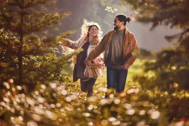 Smiling couple holding hands and walking through an autumnal woodland