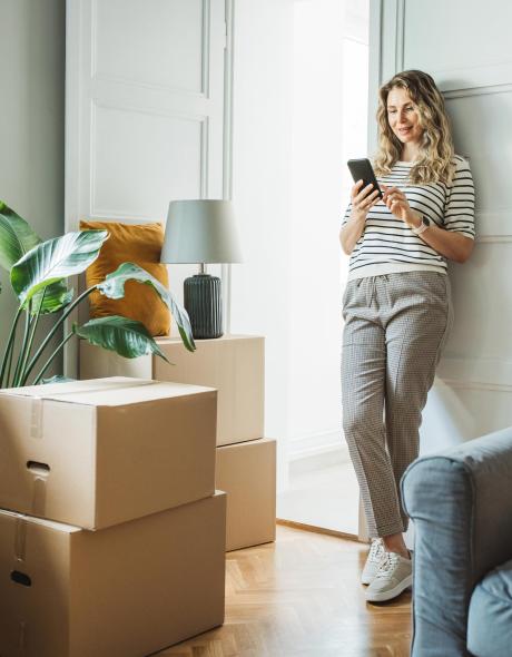 A happy woman enjoying a break on her phone before unpacking moving boxes in her new home